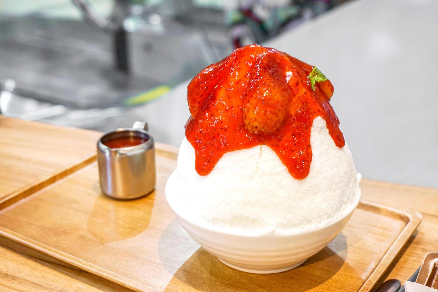 Bingsu strawberry Frozen cow's milk make spinning to snow flake and topped with strawberry syrup. in white ceramic bowl on wooden tray and table with cup stainless photo