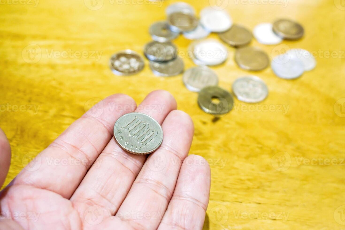 100 Yen Japanese coins on hand with blurry Japanese coins heap on wooden table background. photo