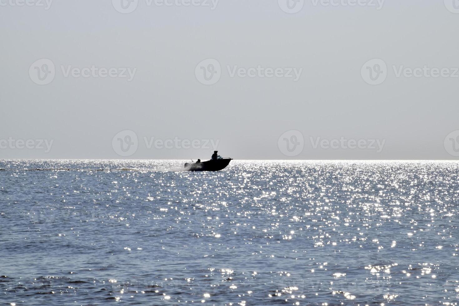 The boat rushes by the sea. In the boat people. Seascape in the evening. Silhouette of a motor boat and people in it against the background of the sea distance photo