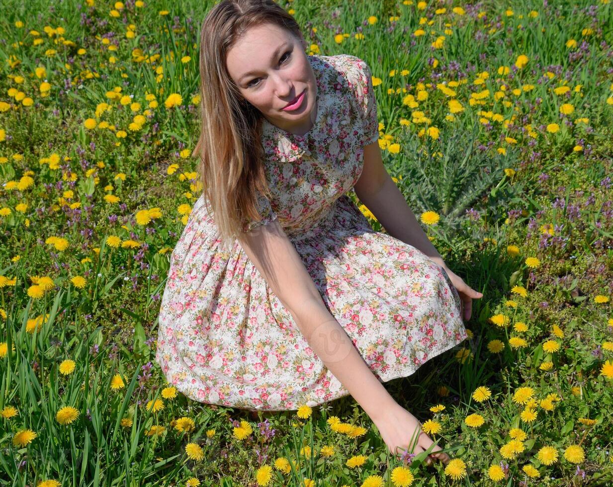 un niña en un vestir en un claro con dientes de león el niña entre el flores foto