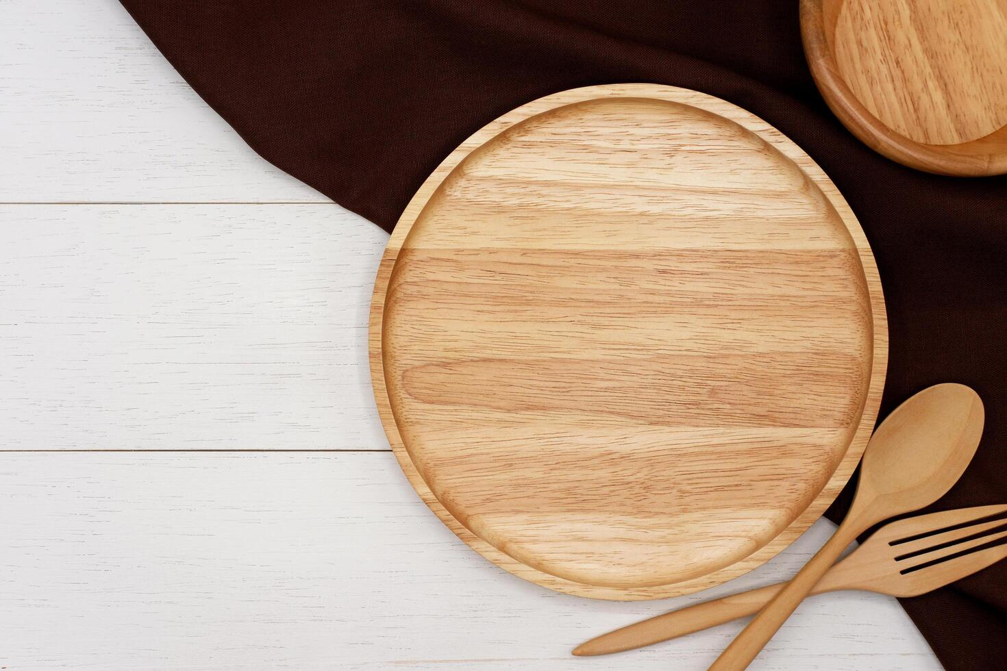 Empty round wooden plate with spoon and fork on white wooden table. Top view image. photo