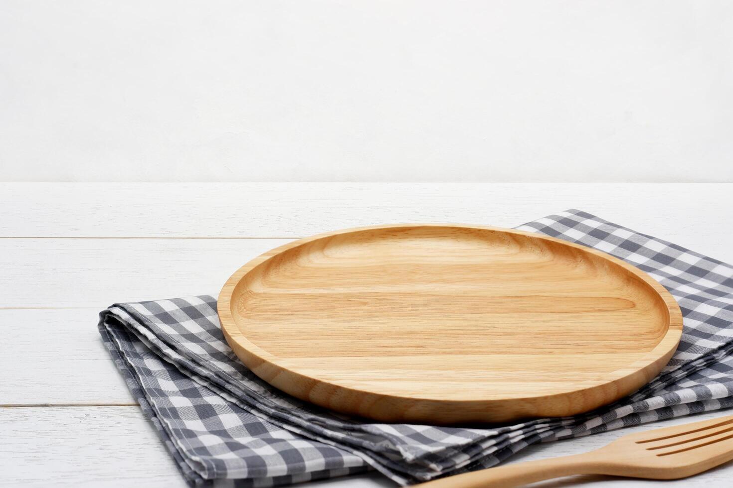 Empty round wooden plate with fork and grey gingham tablecloth on white wooden table. photo