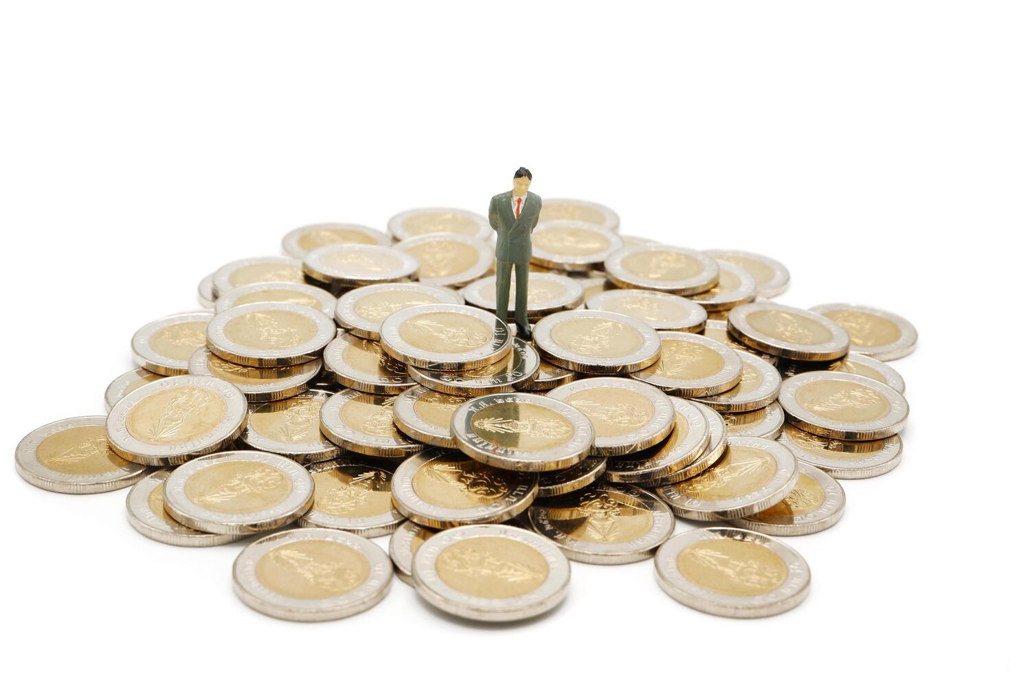 Miniature businessman standing on pile of new 10 Thai Baht coins, isolated on white background. Business concept. photo
