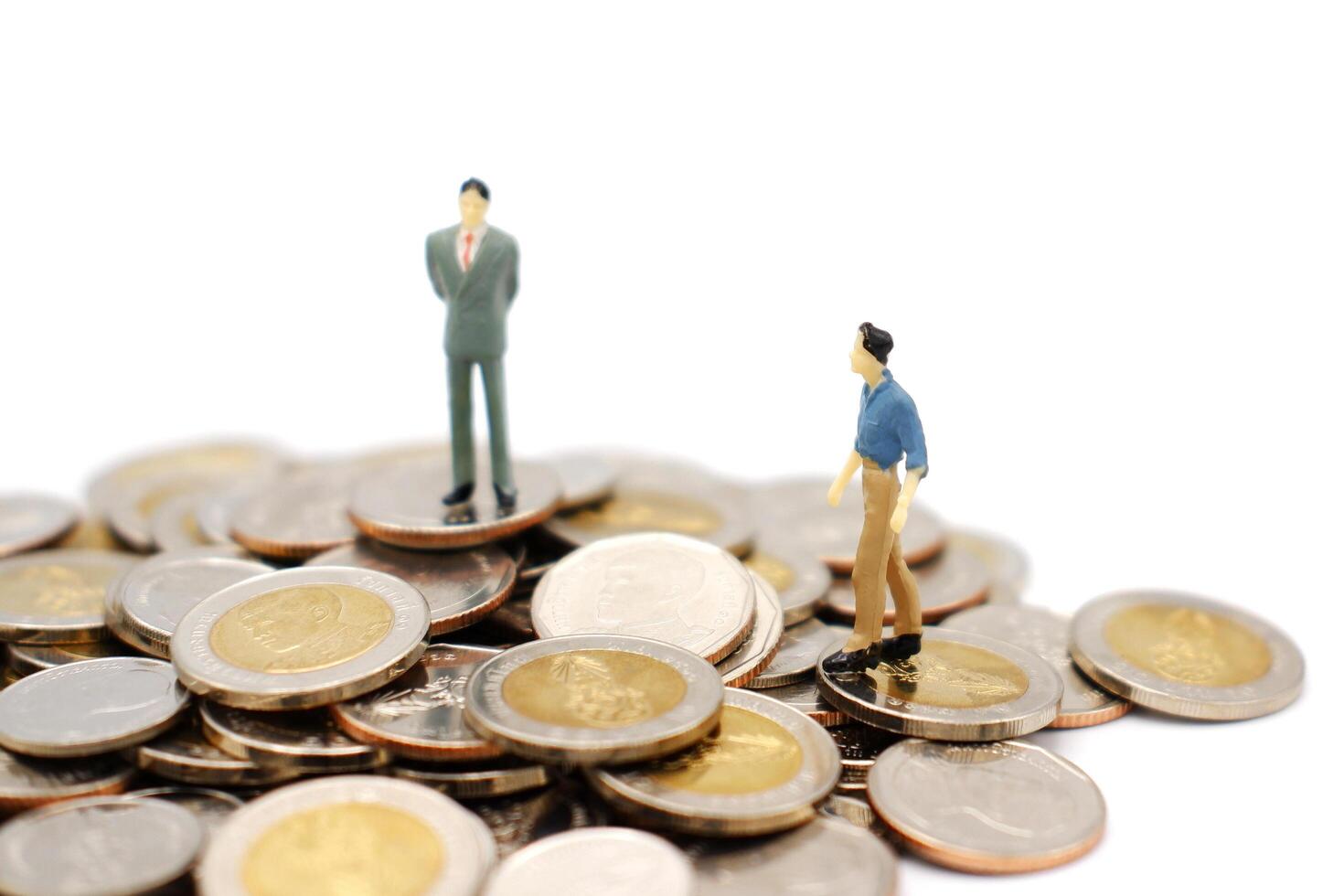 dos miniatura personas caminando y en pie en pila de nuevo tailandés baht monedas, aislado en blanco antecedentes. negocio y Finanzas concepto. foto