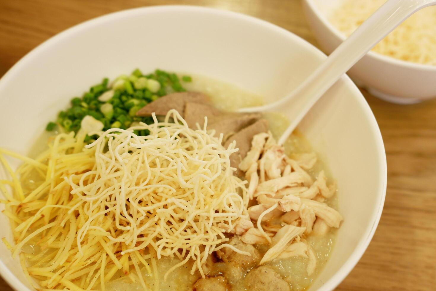 Jok, Thai style rice porridge, with steamed chicken breast, minced pork, pork liver, ginger, spring onion and crispy rice vermicelli noodles. photo