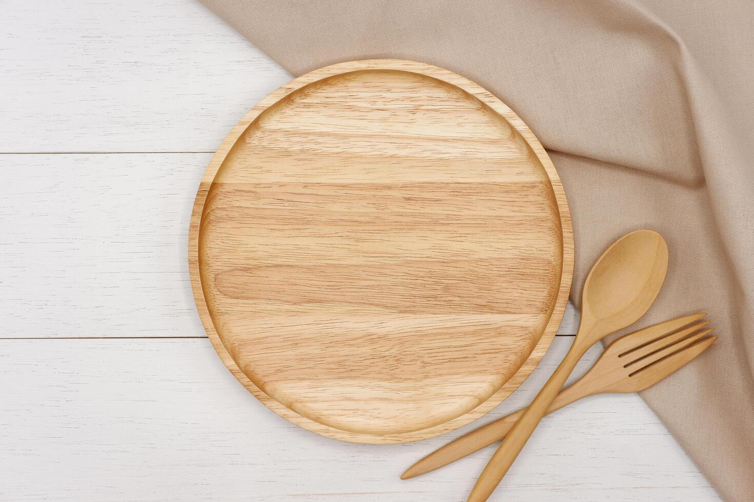 Empty round wooden plate with spoon and fork on white wooden table. Top view image. photo