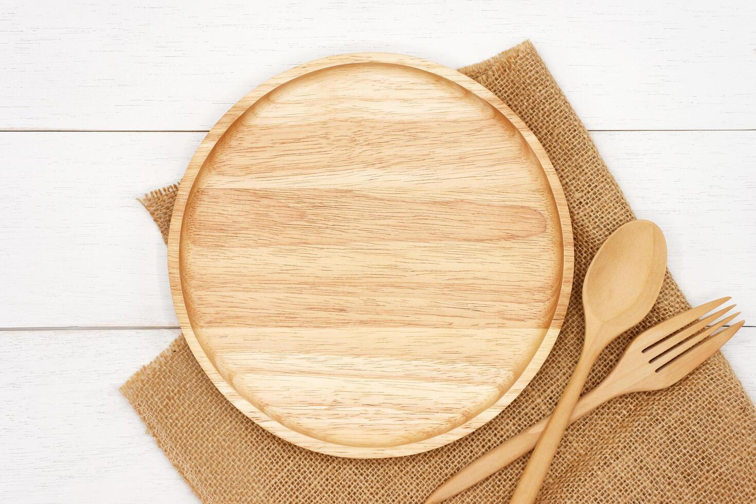 Empty round wooden plate with spoon and fork on white wooden table. Top view image. photo