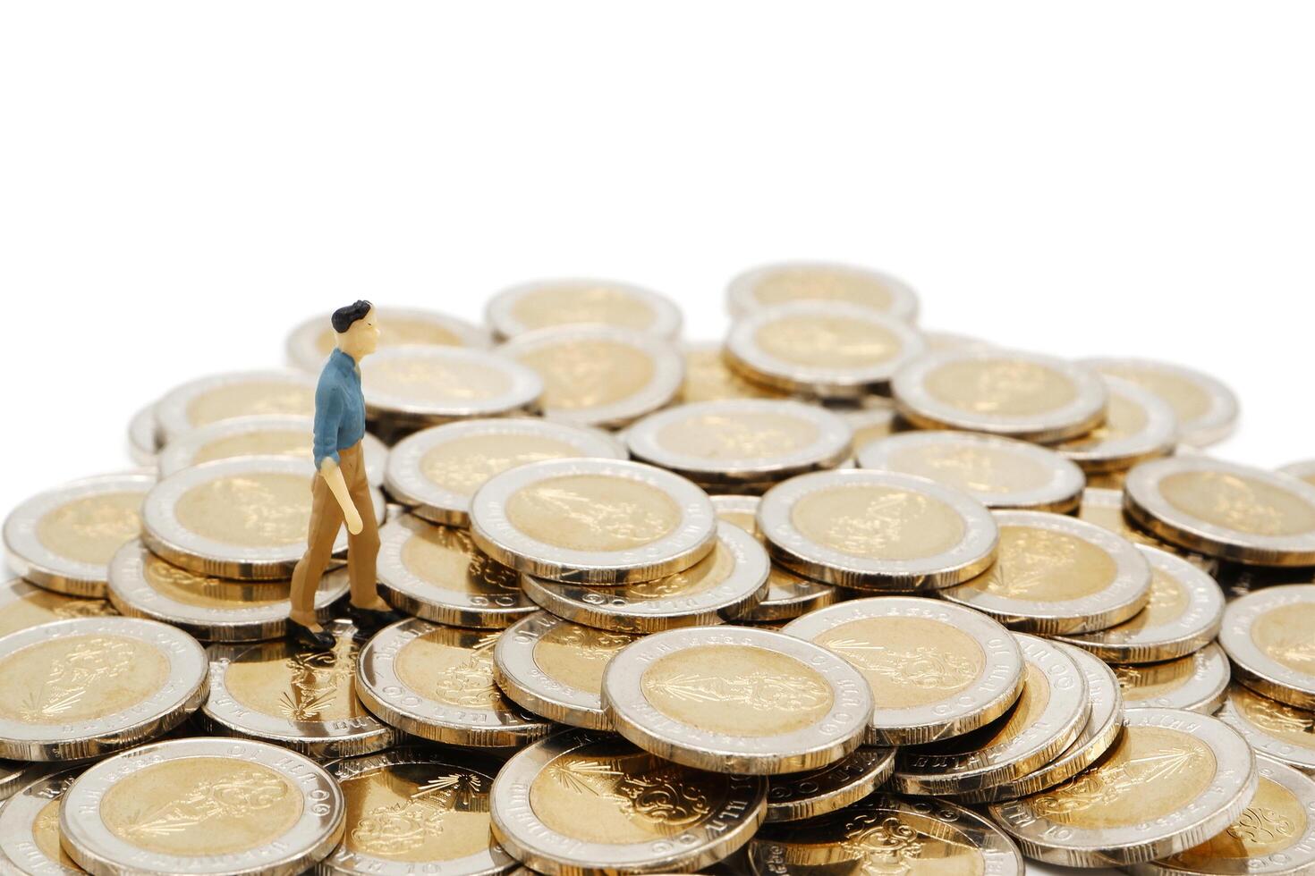 Miniature businessman standing on pile of new 10 Thai Baht coins, isolated on white background. Business concept. photo