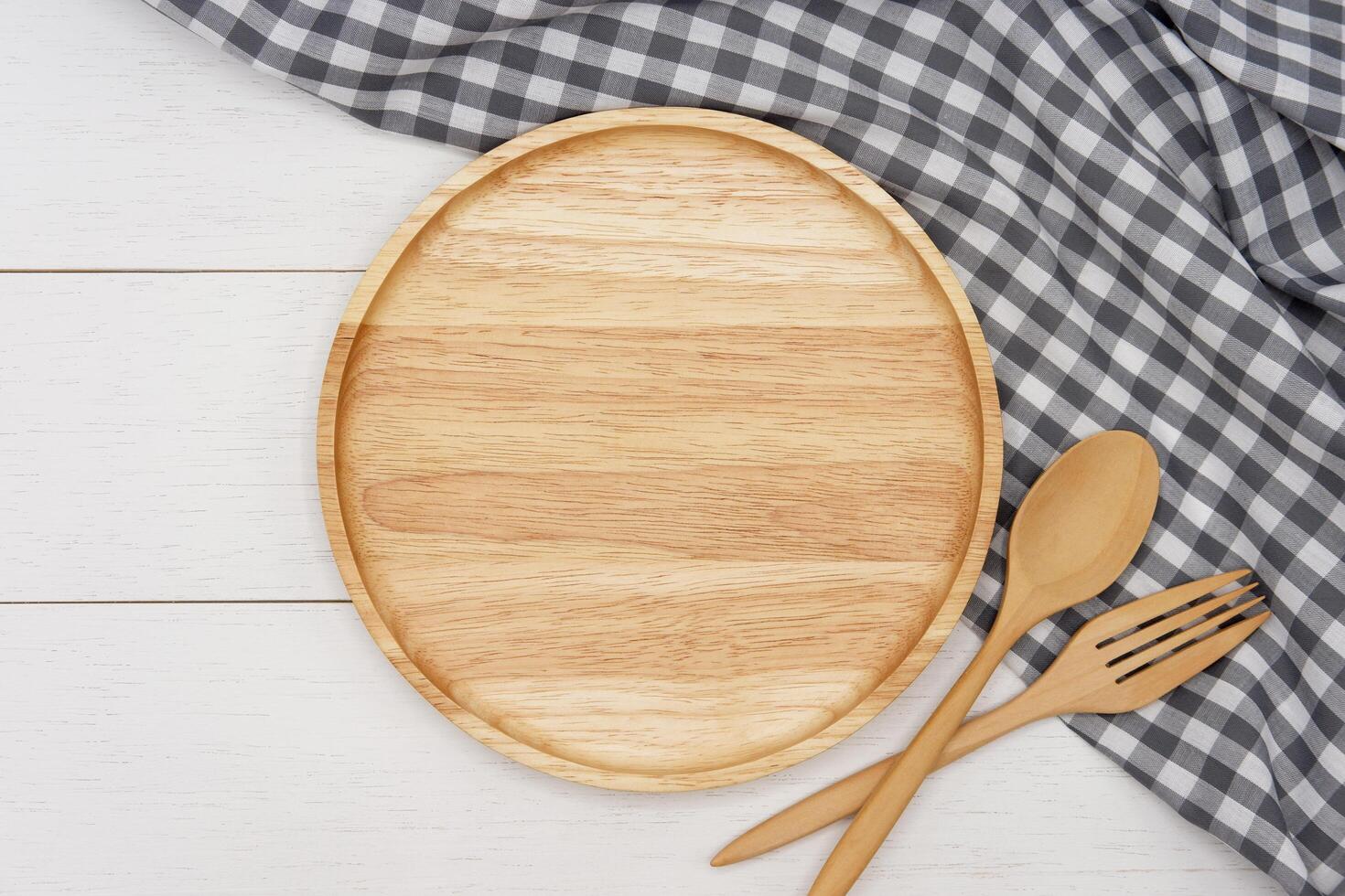 Empty round wooden plate with spoon and fork on white wooden table. Top view image. photo