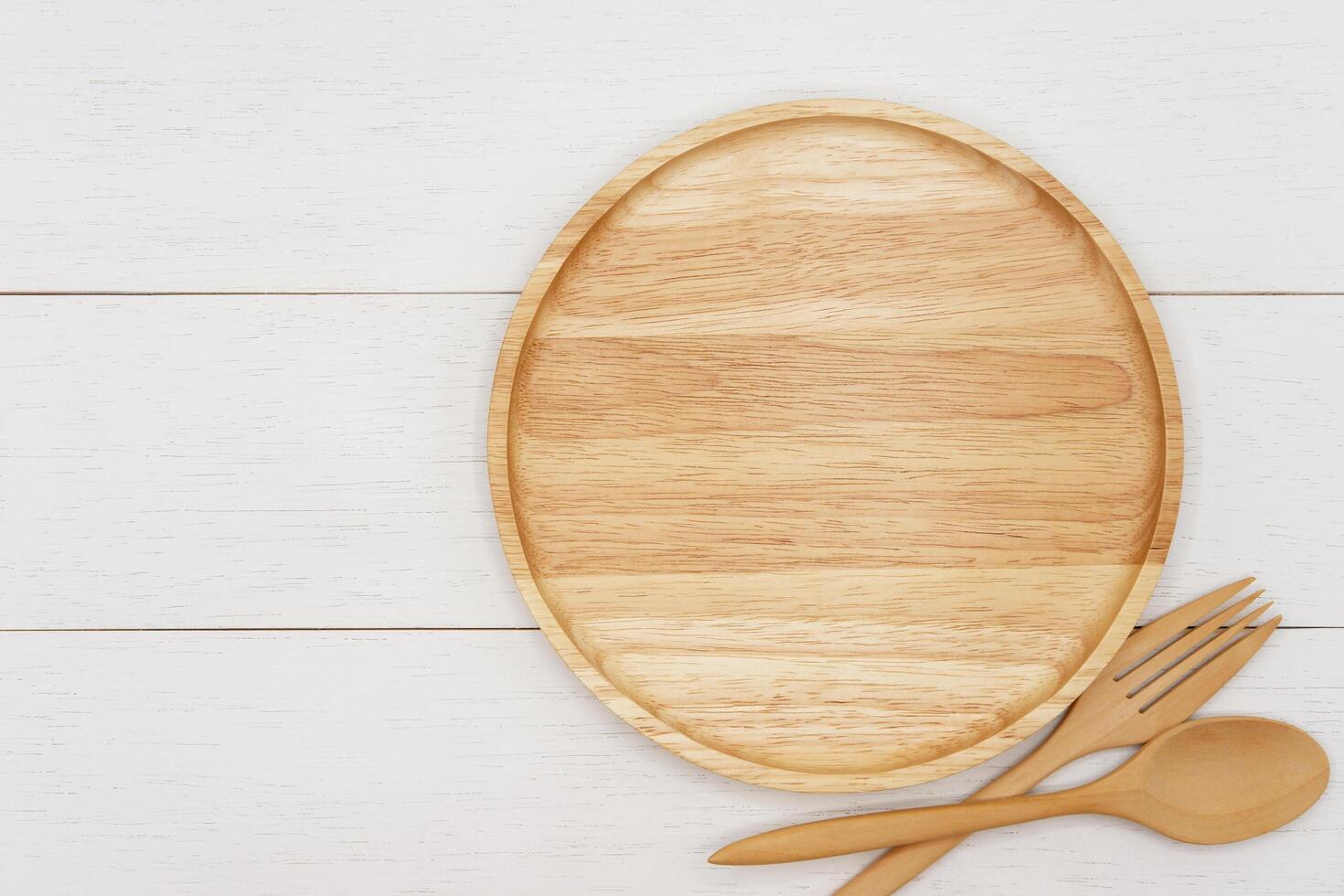 Empty round wooden plate with spoon and fork on white wooden table. Top view image. photo