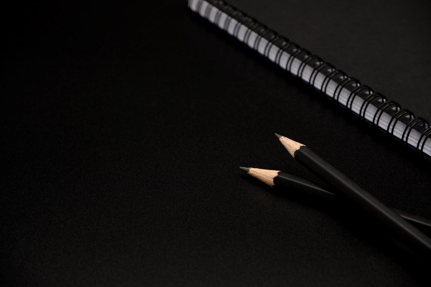 Black pencils with black spiral notebook on black background. photo