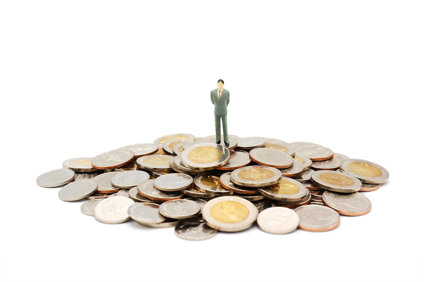 Miniature businessman standing on pile of new Thai Baht coins, isolated on white background. Business and finance concept. photo