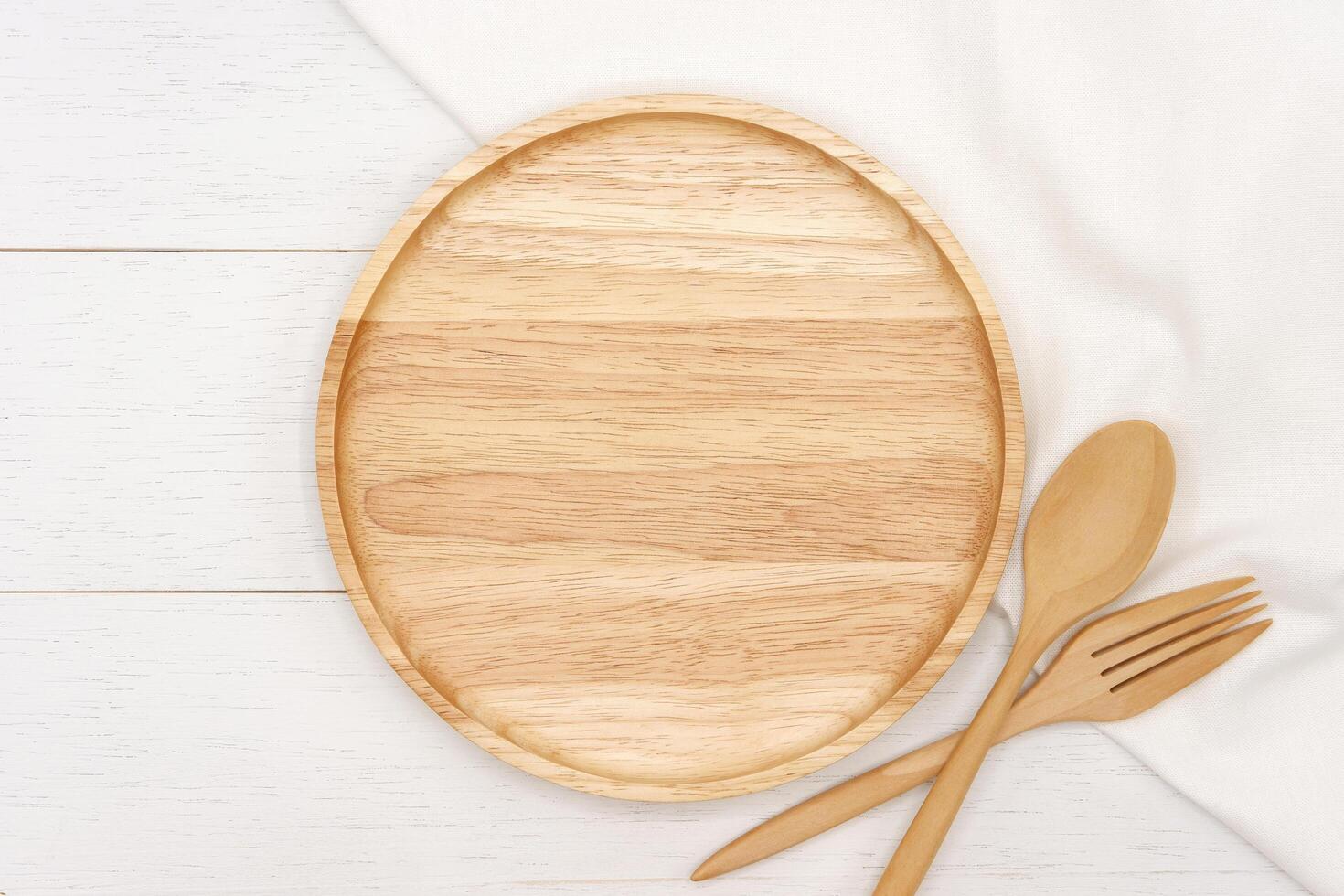 Empty round wooden plate with spoon and fork on white wooden table. Top view image. photo