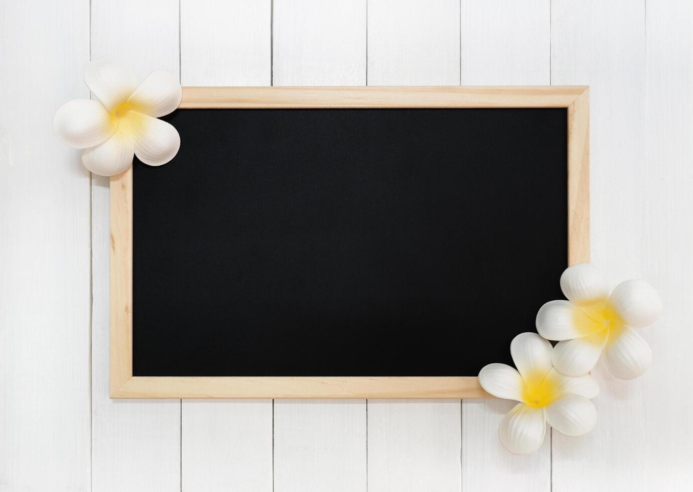 Blank Wooden Chalkboard with the Decor of Artificial White Plumeria Flowers on White Wood Plank Background photo