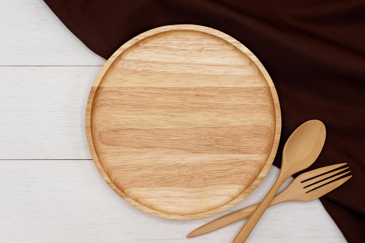 Empty round wooden plate with spoon and fork on white wooden table. Top view image. photo