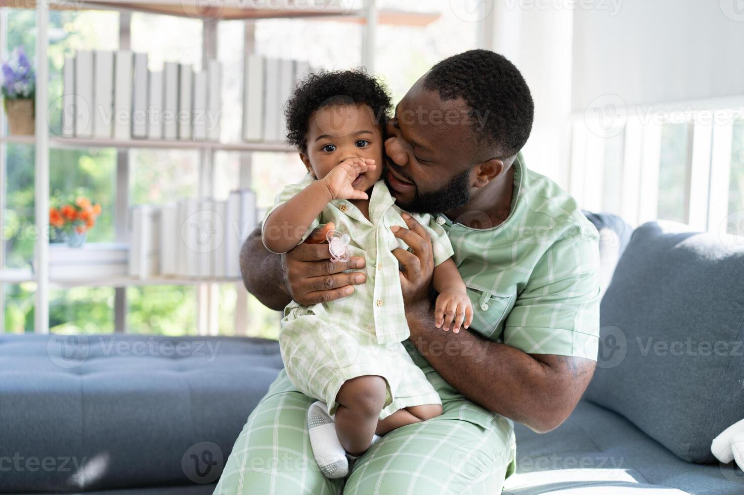 Happy african american man play with little infant toddler child in living room sofa. Parent and little kid relaxing at home. Parents and toddler child girl enjoying spending time at home. Childcare photo