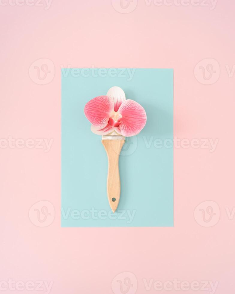 Creative spring and summer layout made with paint brush and beautiful pink orchid flower on pastel pink and blue background. Minimal concept. Trendy paint brush with flowers idea. Nature flat lay. photo