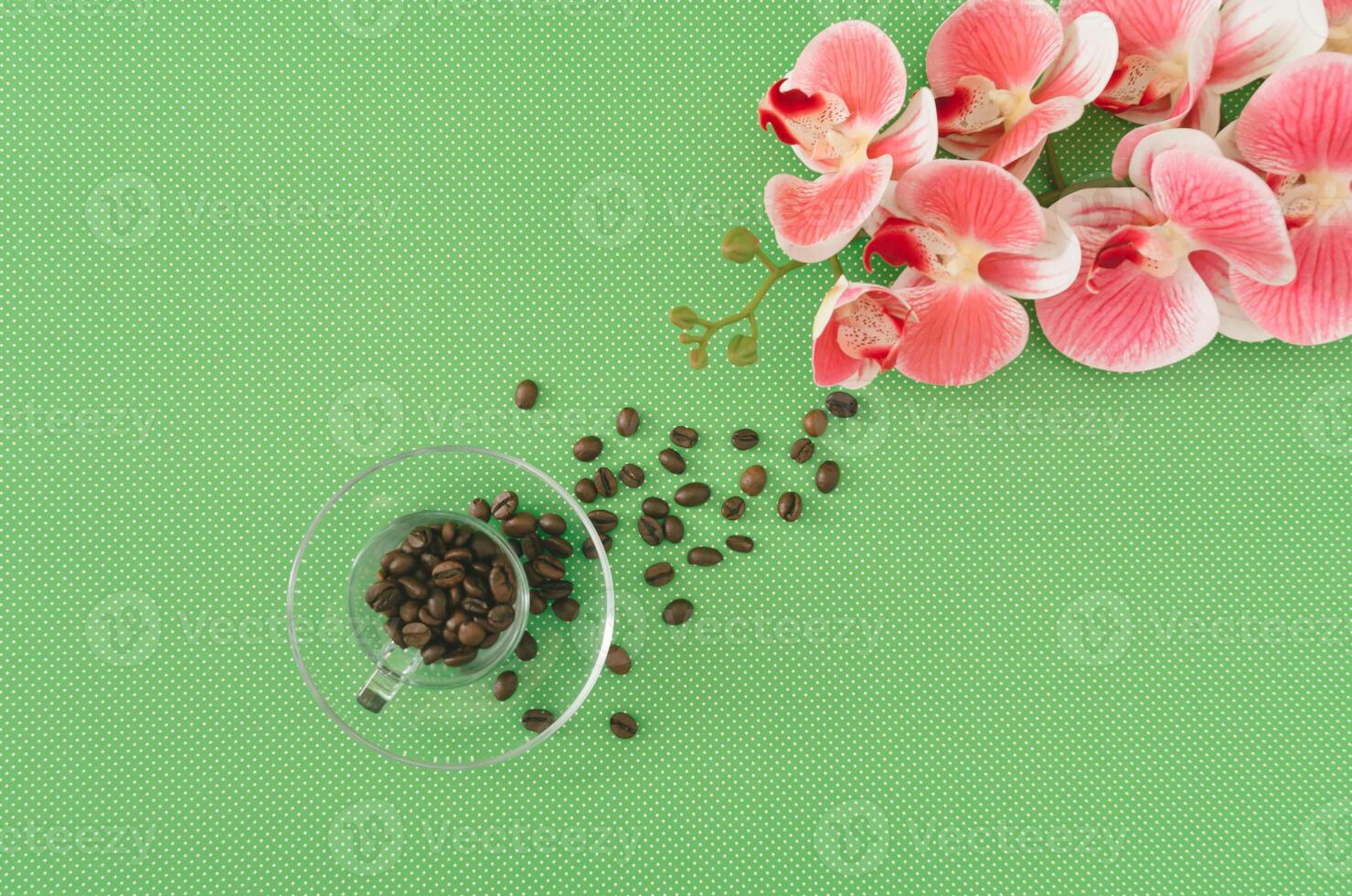Creative spring layout made with coffee cup, roasted coffee beans and beautiful orchid flower on green background. Minimal concept. Trendy coffee with flowers idea. Spring aesthetic. Flat lay. photo