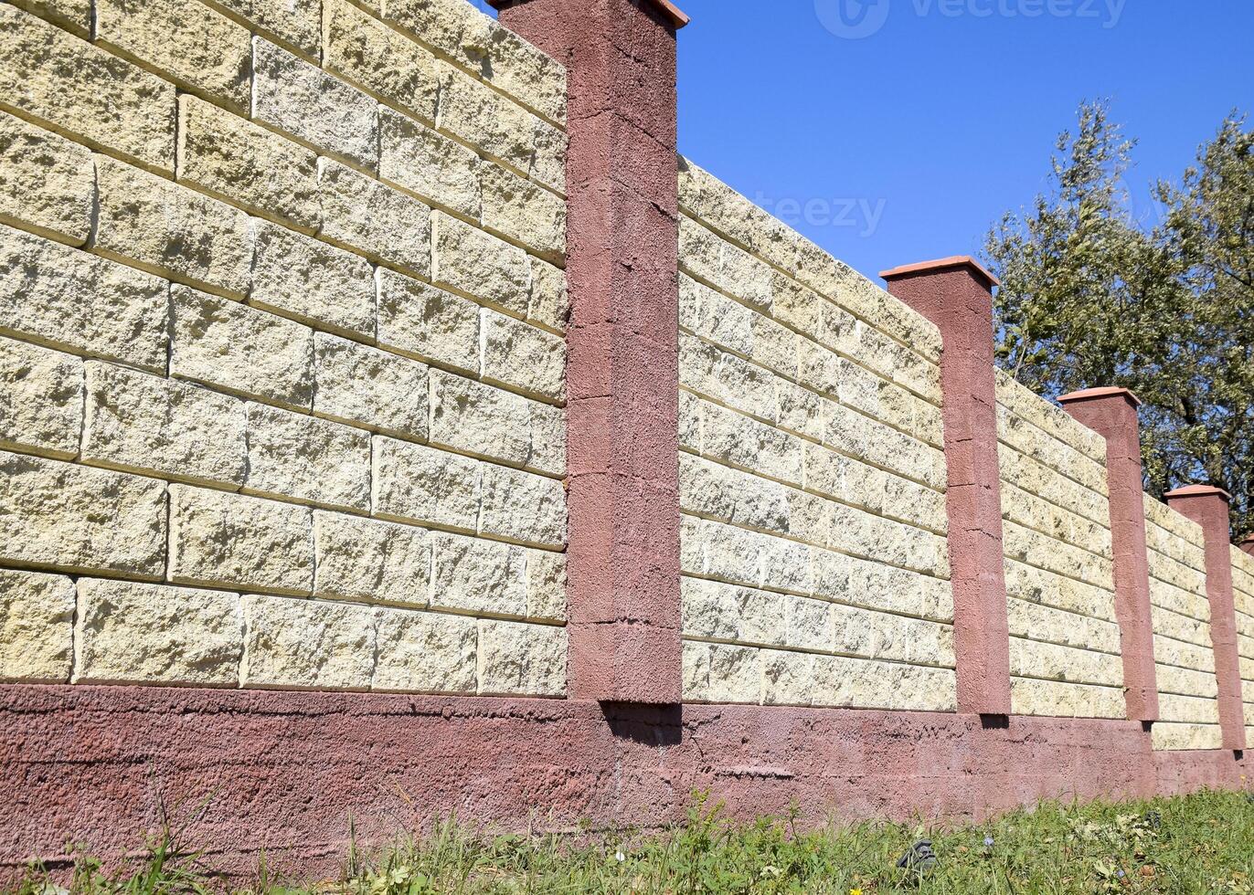 Fence made of bricks and decorative plaster. Yellow fence with red elements. High and beautiful fencing photo