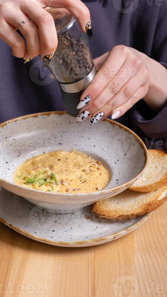 un mujer vierte pimienta dentro un plato de queso crema sopa con nueces y verduras. foto