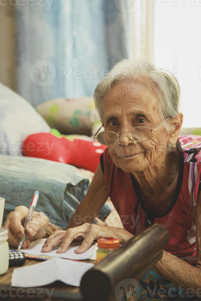 old asian woman writing wording on white paper at home living room photo