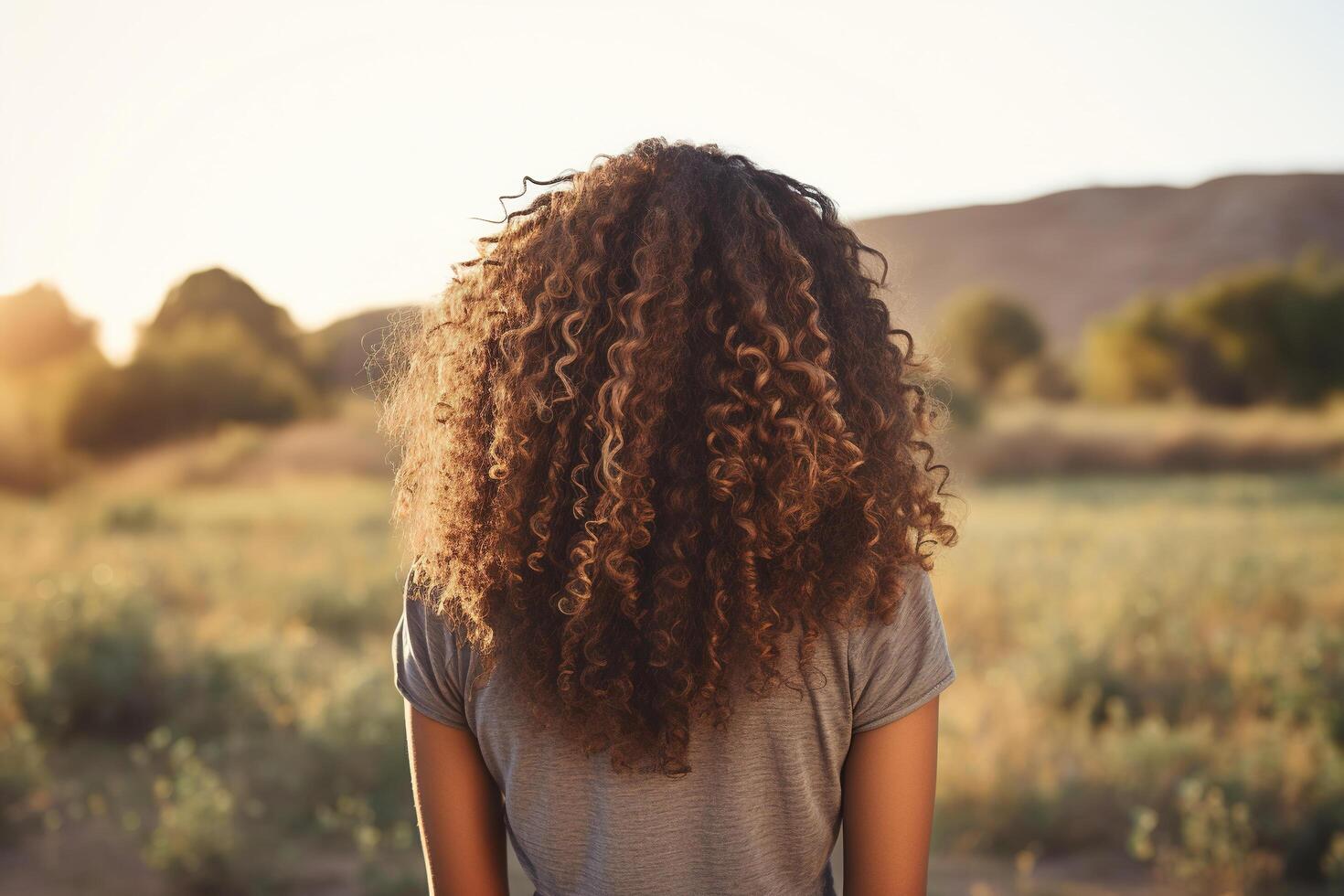 AI generated An attractive dark-skinned young woman with curly hair stands backwards in the nature. Generated by artificial intelligence photo