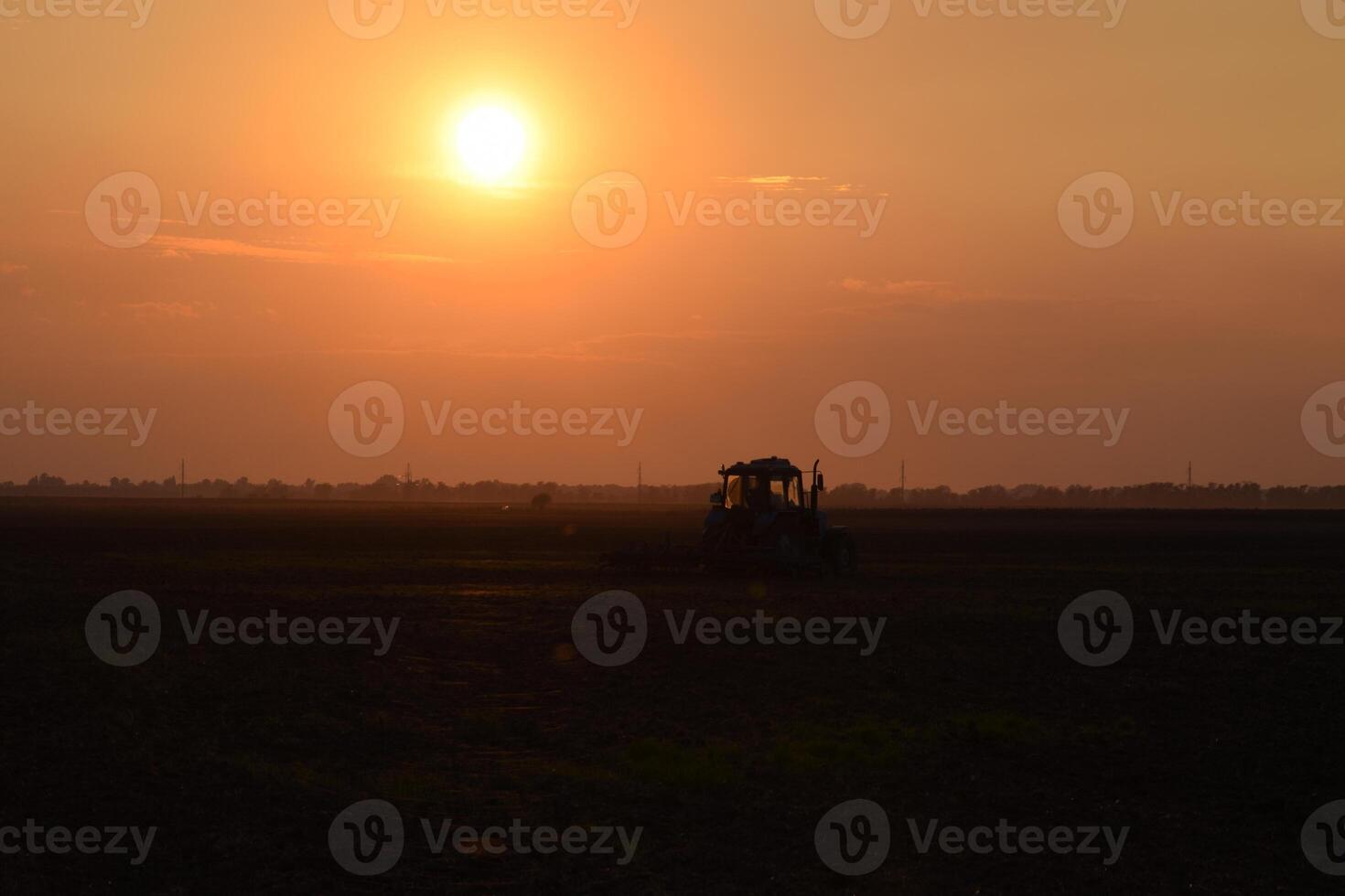 Tractor plowing plow the field on a background sunset. tractor silhouette on sunset background photo