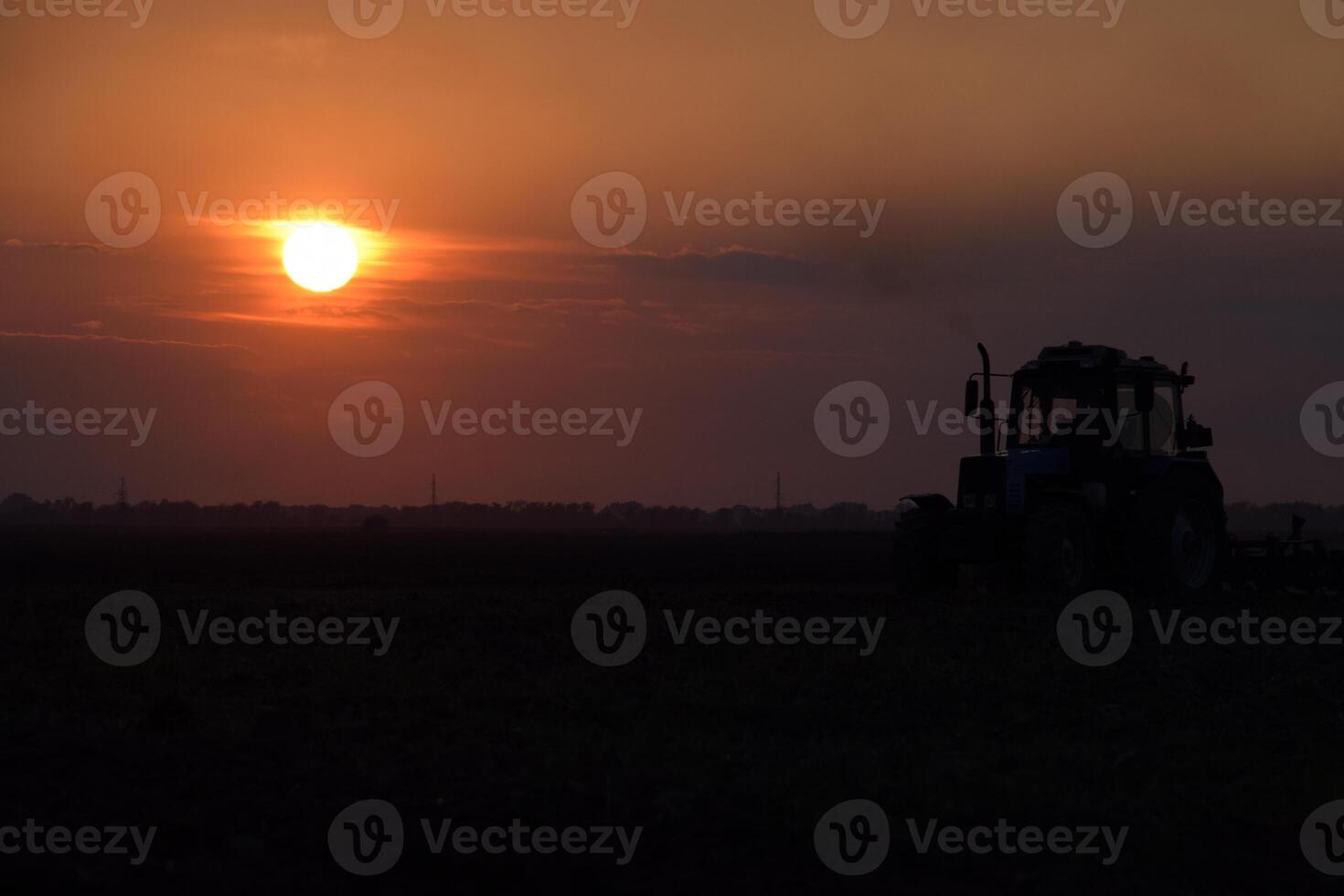 Tractor plowing plow the field on a background sunset. tractor silhouette on sunset background photo