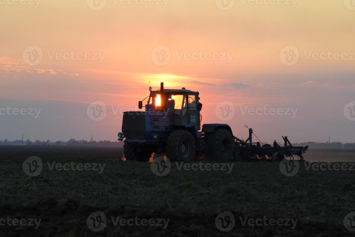 Tractor plowing plow the field on a background sunset. tractor silhouette on sunset background photo