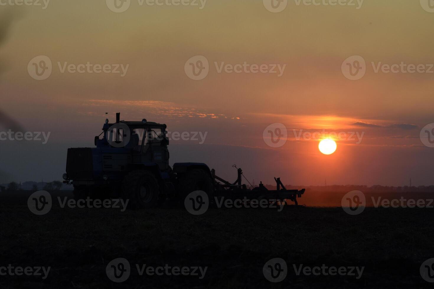Tractor plowing plow the field on a background sunset. tractor silhouette on sunset background photo