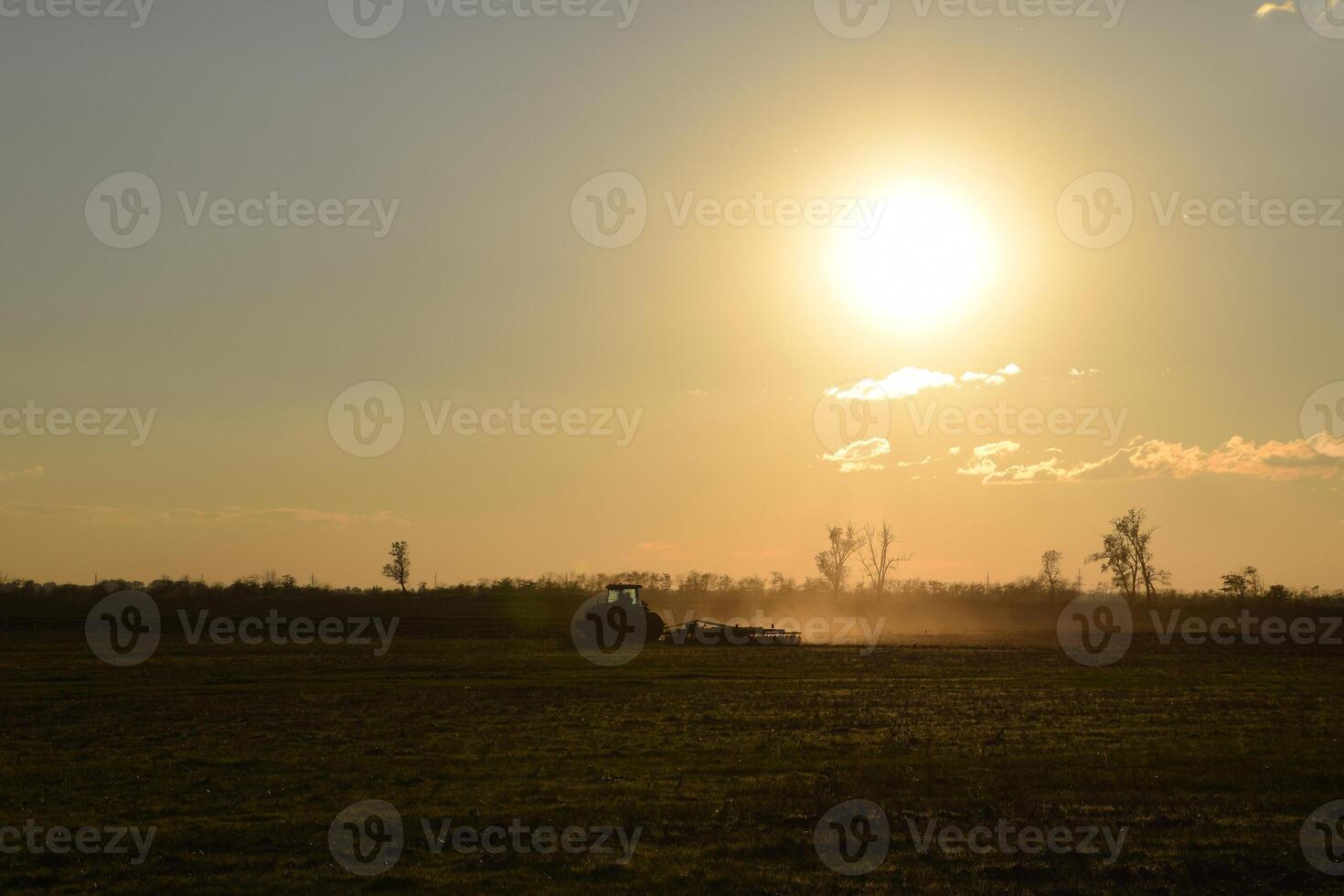 Tractor at sunset plow plow a field. Tilling the soil in the fall after harvest. The end of the season photo
