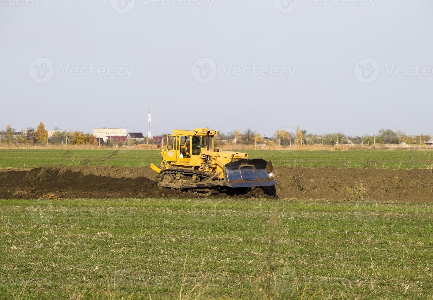 el amarillo tractor con adjunto grederom hace suelo arrasamiento. foto