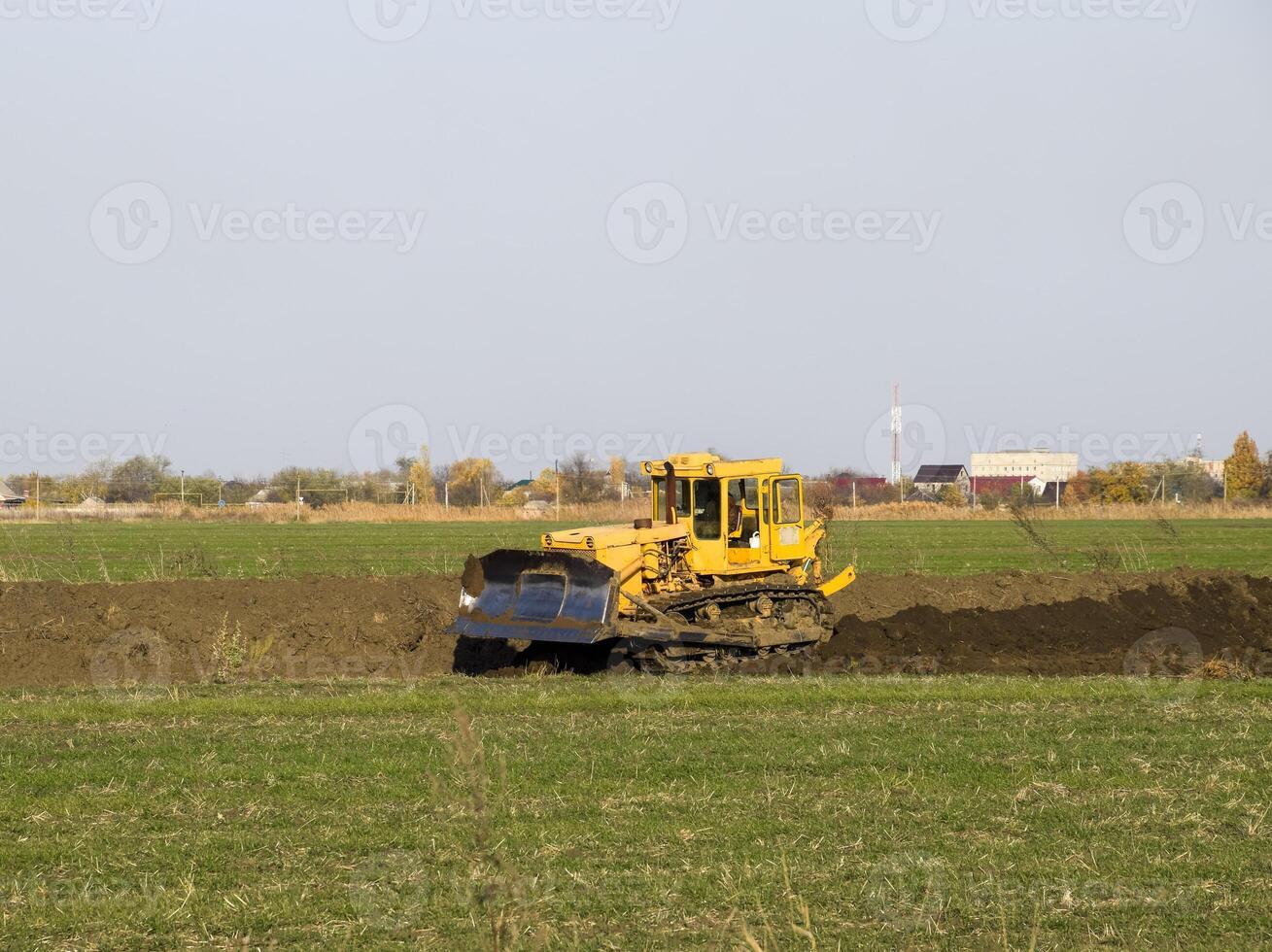 The yellow tractor with attached grederom makes ground leveling. photo