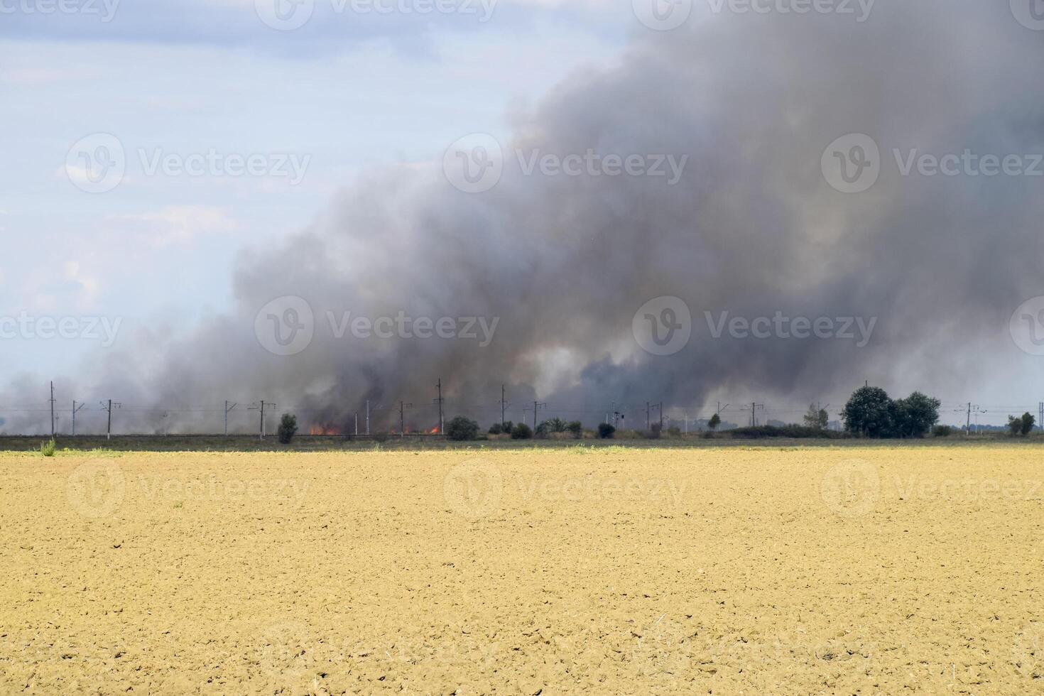 The fire is somewhere beyond the plowed field. Dark smoke from a fire. photo