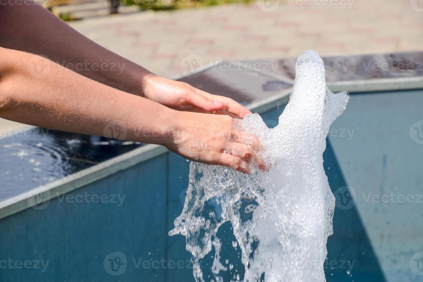 mano toque el fuente. un corriente de agua desde el fuente es tocado por mano foto