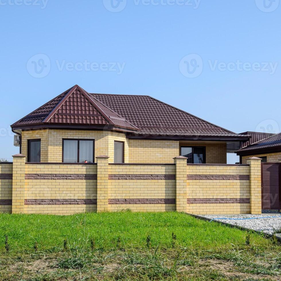 Brick house with a fence and gates. View of a new built-up fence and a house made of bricks and corrugated metal. photo