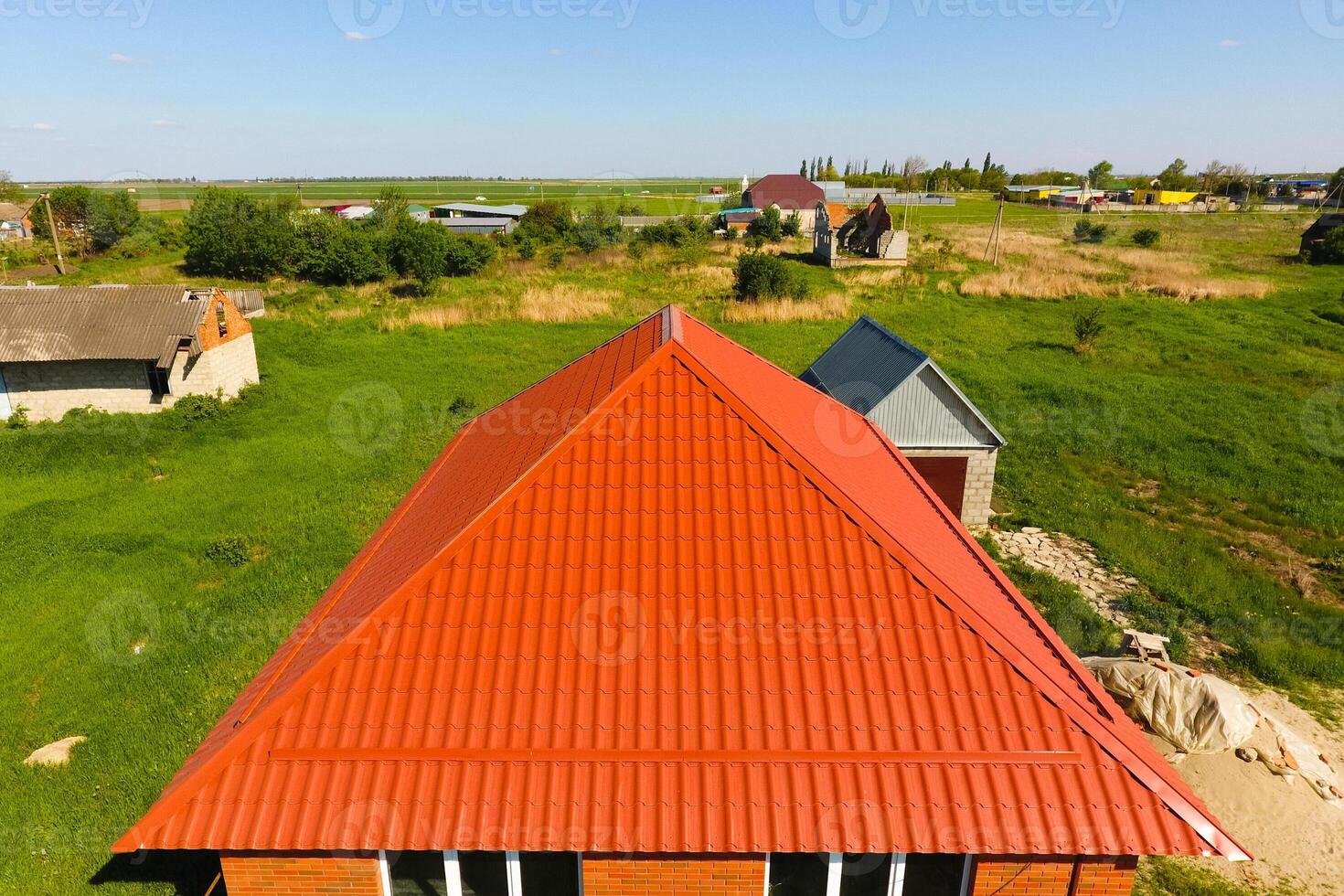 House with an orange roof made of metal, top view. Metallic profile painted corrugated on the roof. photo