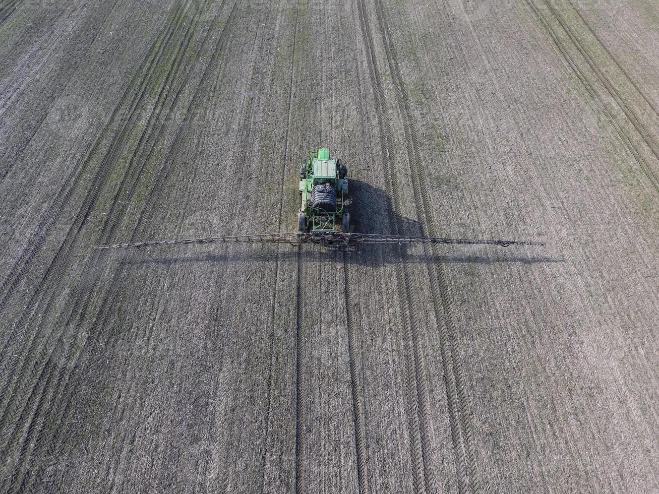 Tractor with hinged system of spraying pesticides. Fertilizing with a tractor, in the form of an aerosol, on the field of winter wheat. photo