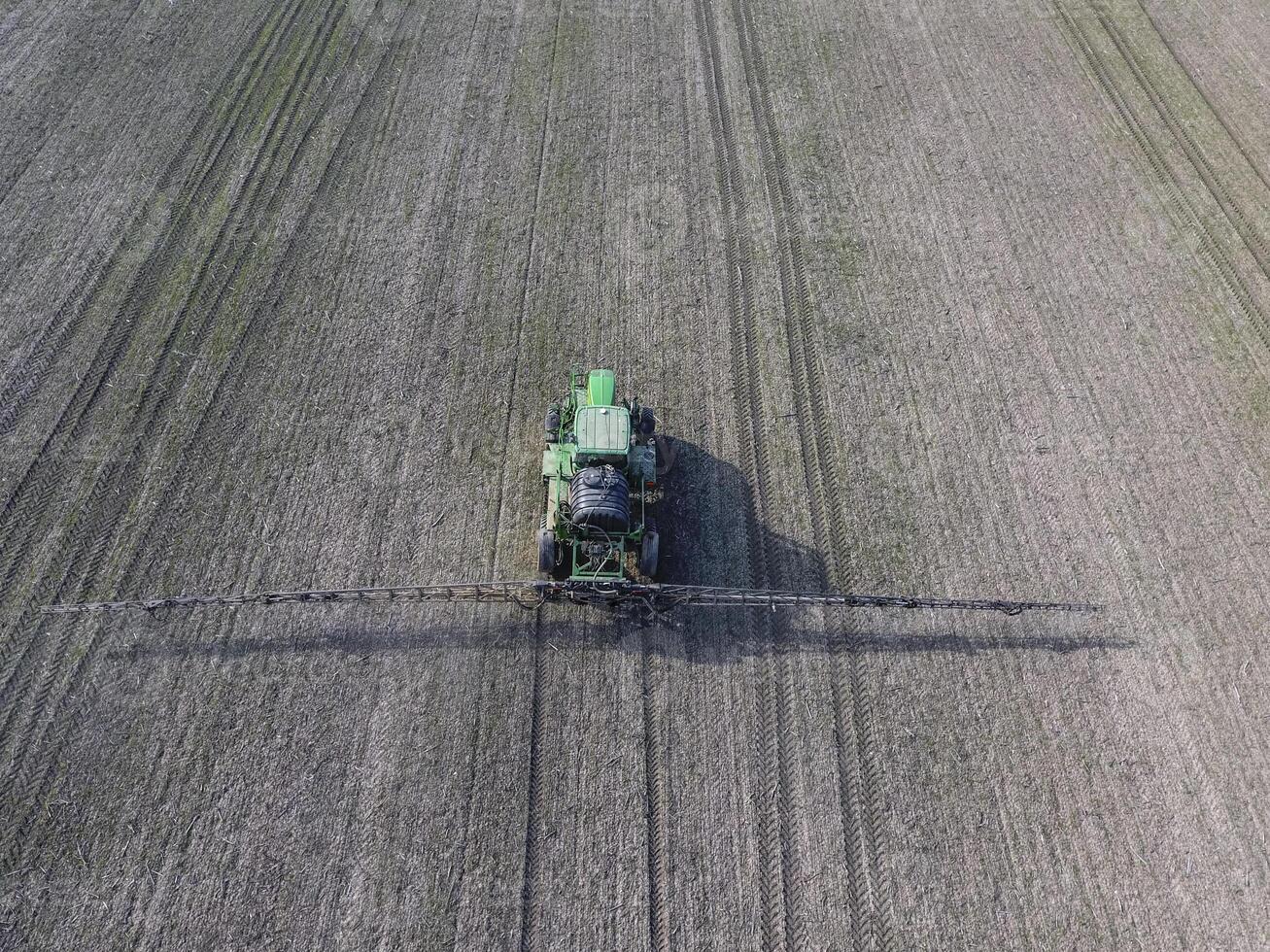 Tractor with hinged system of spraying pesticides. Fertilizing with a tractor, in the form of an aerosol, on the field of winter wheat. photo