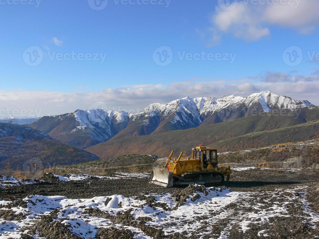 Crawler tractor with grederom against the backdrop of snow-capped mountains photo