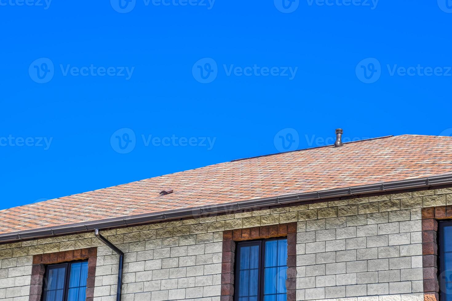 The house is made of beige bricks, the roof is covered with bitumen shingles. Metal plastic windows on the house. photo