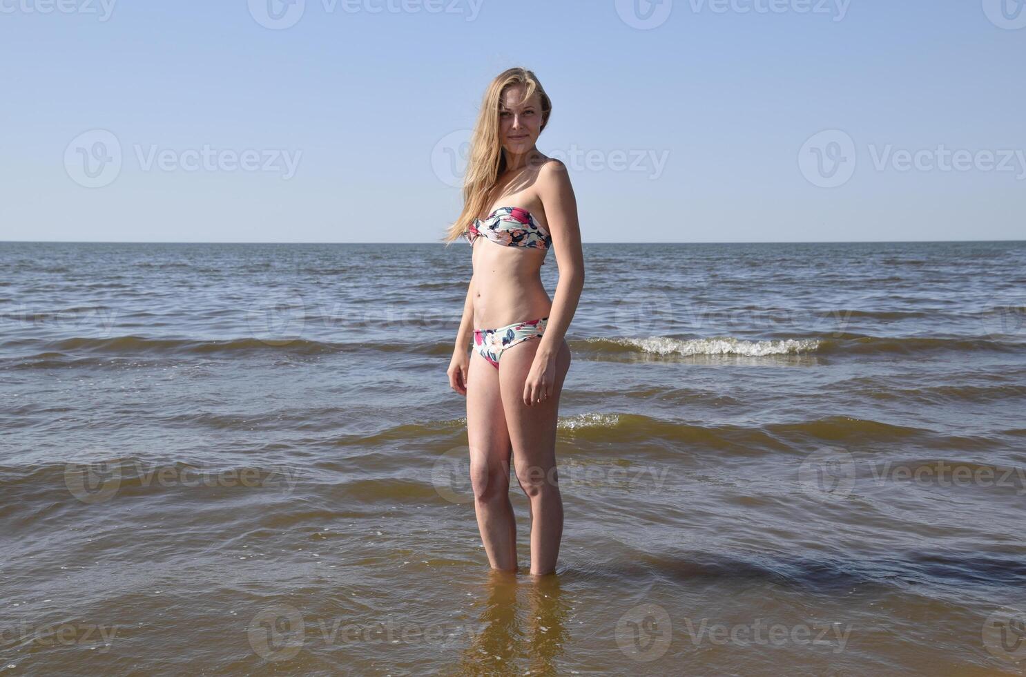 Blond girl in a bikini on the beach. Beautiful young woman in a colorful bikini on sea background photo