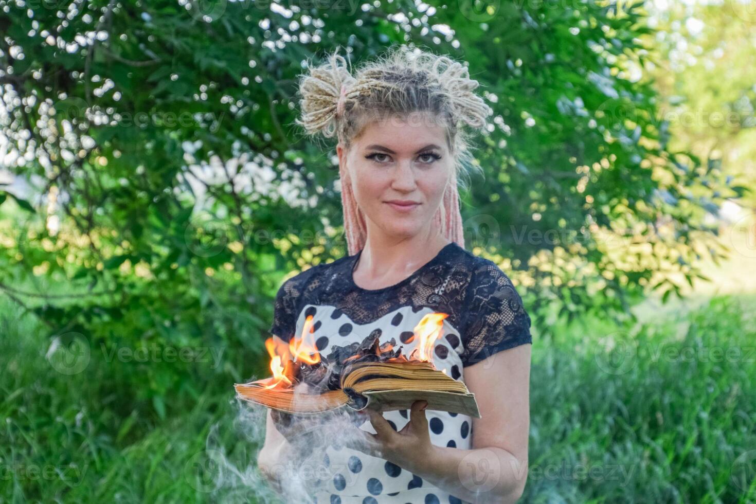 girl holds a burning book in her hands. A young woman in a forest burns a book. photo