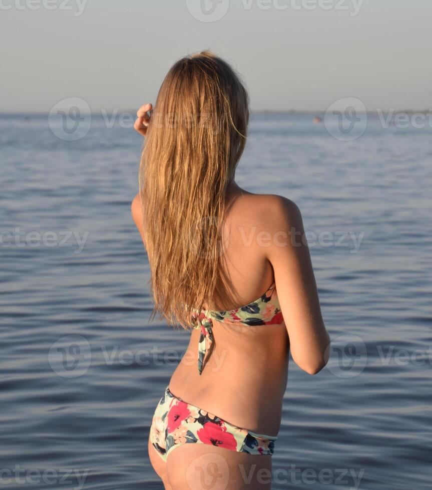 Blond girl in a bikini standing in the sea water. Beautiful young woman in a colorful bikini on sea background photo