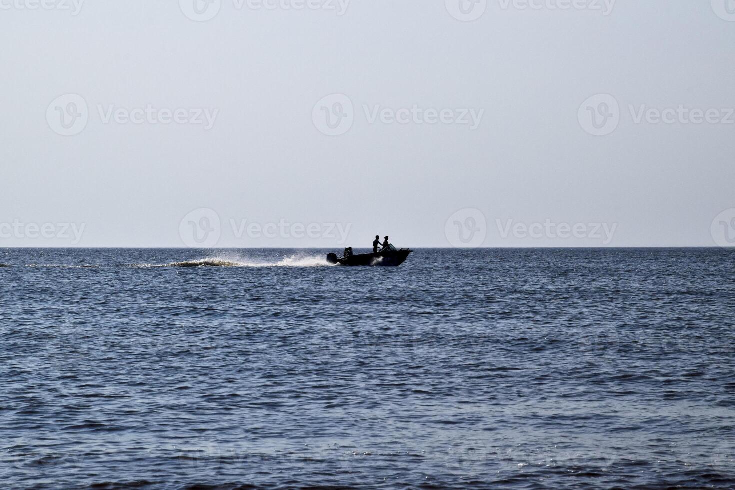 The boat rushes by the sea. In the boat people. Seascape in the evening. Silhouette of a motor boat and people in it against the background of the sea distance photo