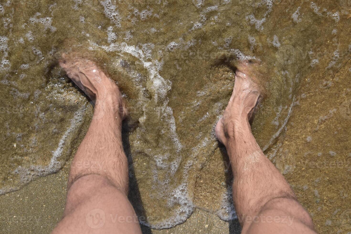 Legs men on the sea sand near sea wave photo