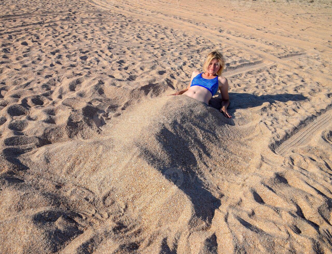 niña en un bikini en el playa enterrado en medio en el arena. foto