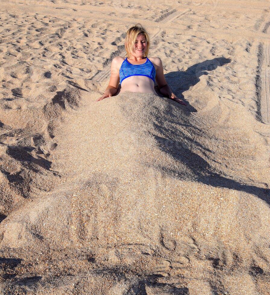 Girl in a bikini on the beach buried in half in the sand. photo