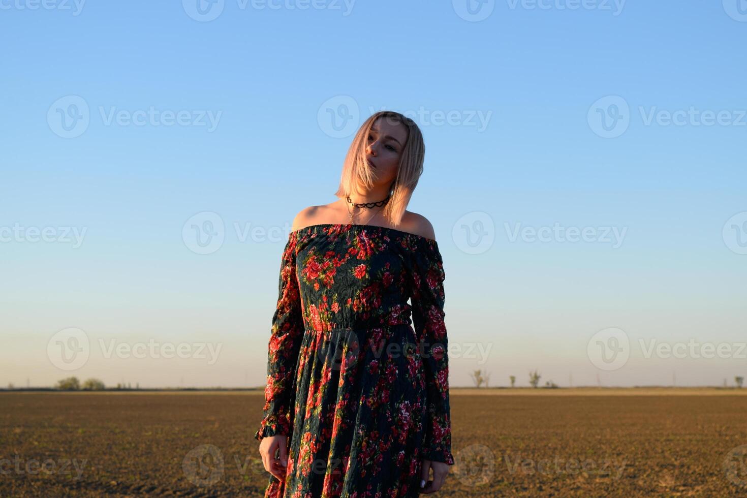 Woman in a plowed field in a red-black dress on a sunset background. photo