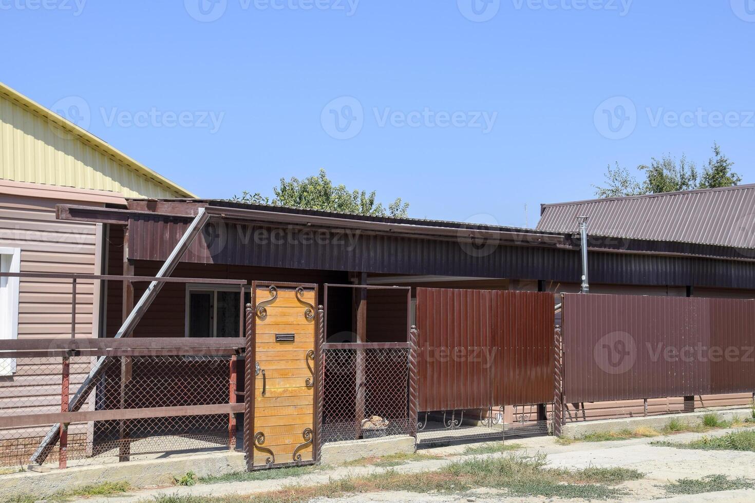 Brick house with a fence and gates. View of a new built-up fence and a house made of bricks and corrugated metal. photo